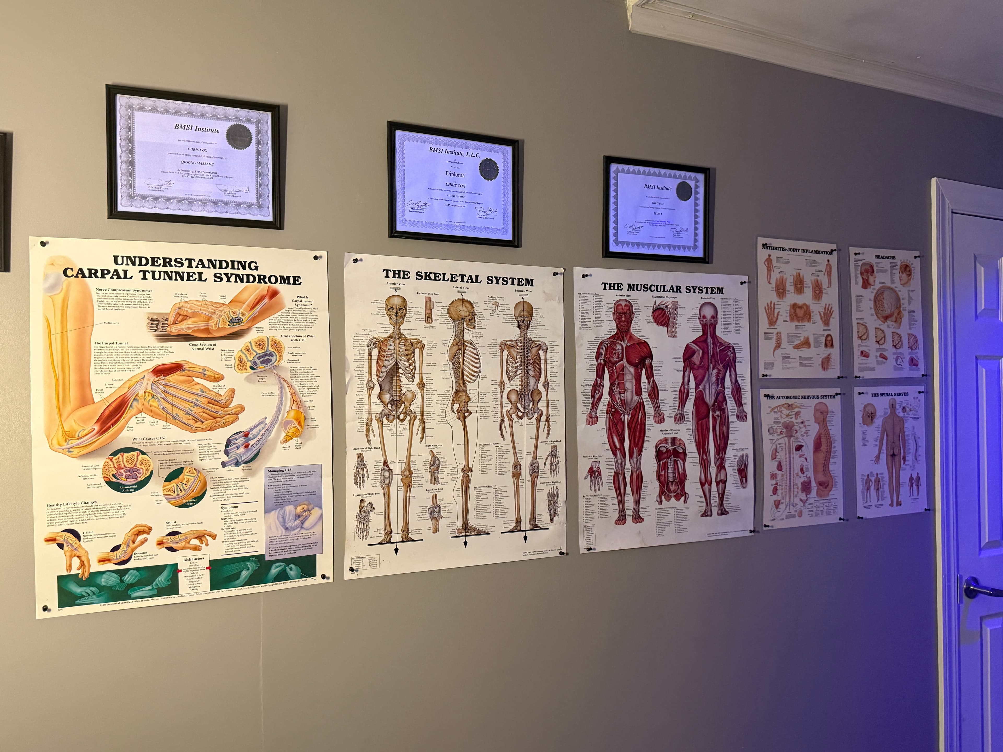 Anatomy charts and massage therapy training certificates on the treatment room wall