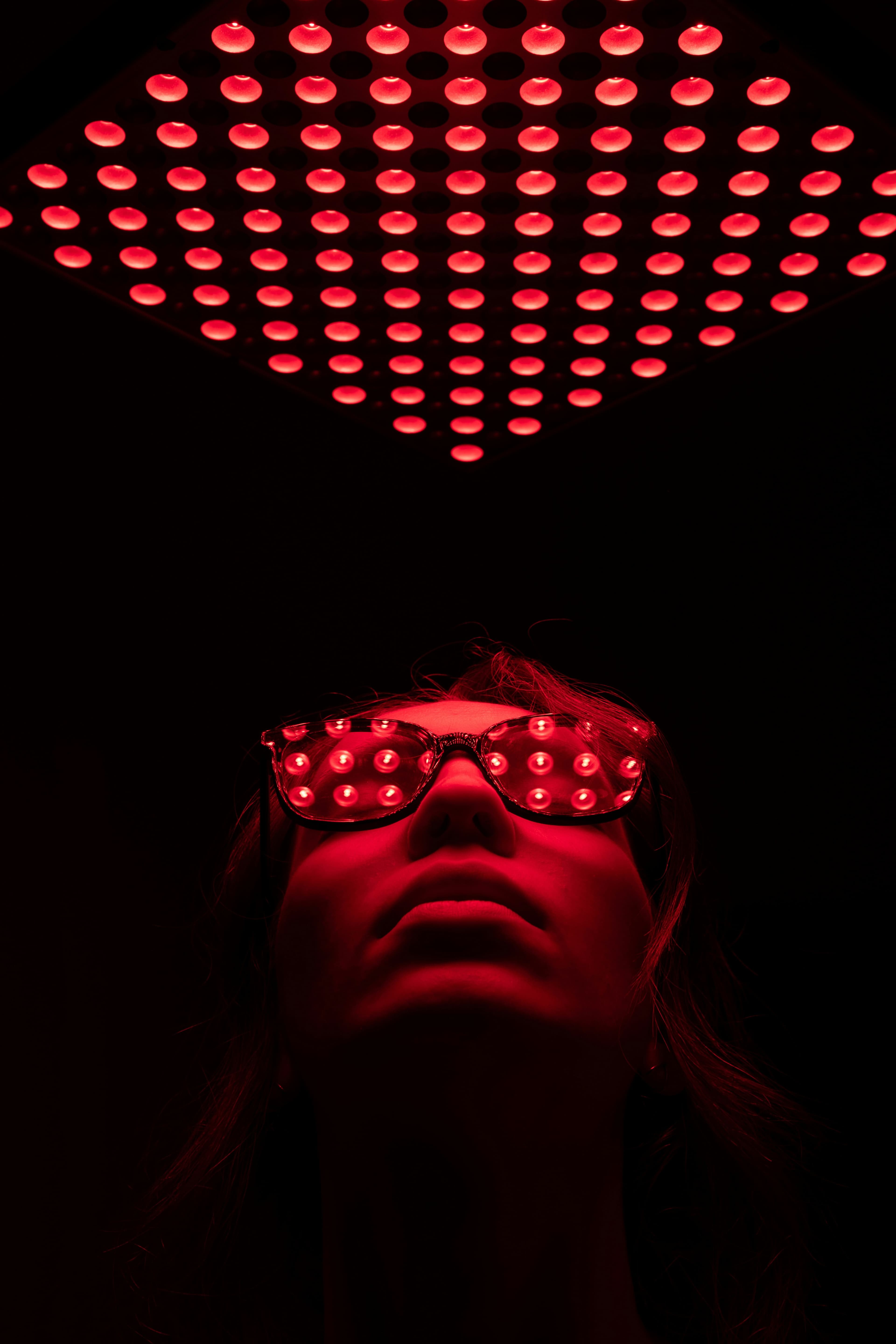 Red light therapy panel glowing above a client wearing protective glasses